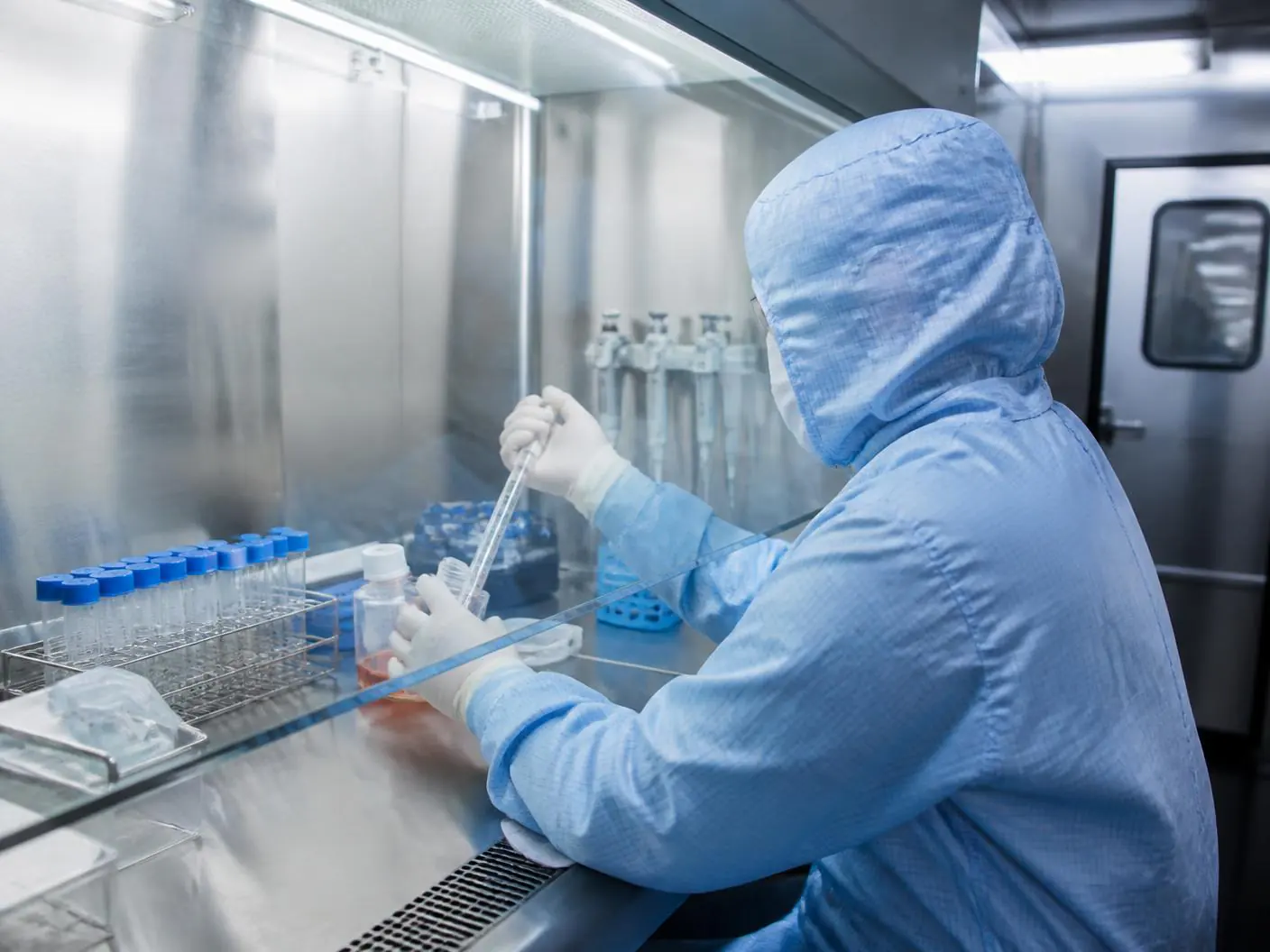 A technician in cleanroom gowning working at a biosafety cabinet in a licensed laboratory.